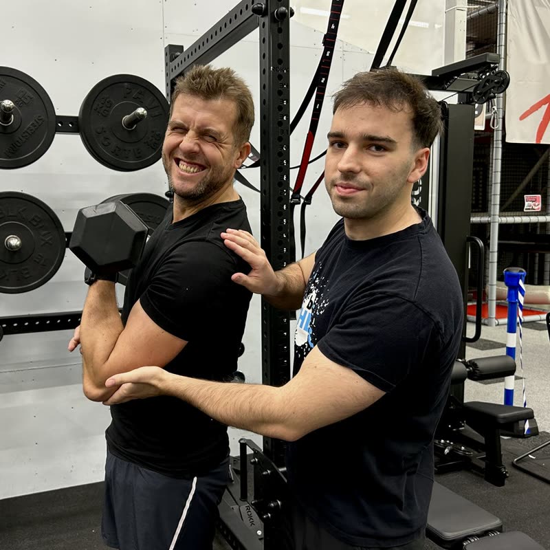 Uśmiechnięty klient z hantlą i trener Athletic Spot w studiu na Zawiłej